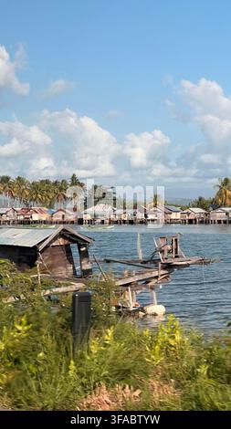 Traditionelle Pfahlhäuser säumen ein tropisches Uferdorf in Sulawesi, Indonesien, umgeben von ruhigem Meer und Kokospalmen. Stockfoto