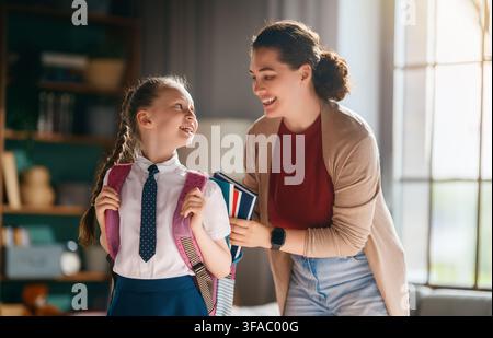 Fröhlicher Morgenmoment, in dem eine liebevolle Mutter ihre Tochter in Schuluniform ermutigt, bevor sie zur Schule geht. Die Szene fängt die Wärme der Eltern Stockfoto