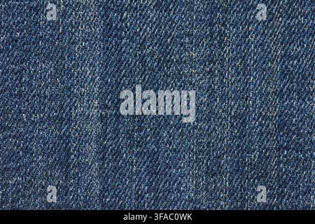 Blauer Denimstoff mit ausgebleichten, gesprenkelten Bereichen, die das Bild ausfüllen, zeigt eine abgenutzte Köperbindung, unregelmäßige Tonvariationen und eine robuste Textur in einer detaillierten Nahaufnahme. Stockfoto