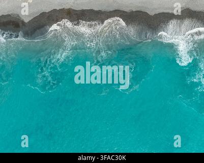 Luftaufnahme von türkisfarbenen Meereswellen, die auf den dunklen Kiesstrand von Madeira, Portugal, krachen Stockfoto