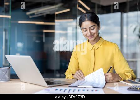 Eine junge indische Frau sitzt an einem Schreibtisch in einem Büro und unterschreibt Dokumente. Stockfoto