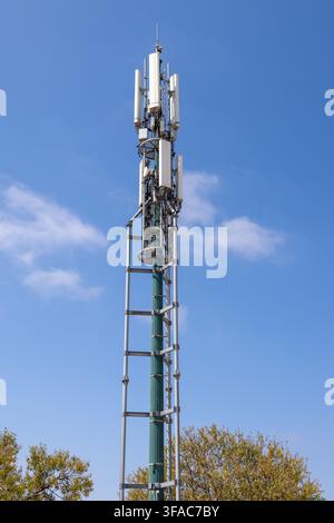 Ein hoher Telekommunikationsmast, der mit mehreren Antennen ausgestattet ist, steht vor einem hellblauen Himmel mit vereinzelten weißen Wolken Stockfoto