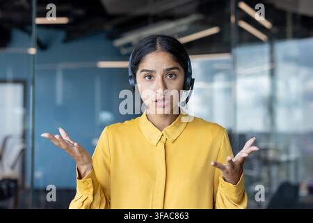 Nahaufnahme-Porträt einer jungen indischen Frau mit Headset, die in einem Büro vor einer Kamera sitzt und ein Online-Gespräch per Videoanruf führt. Stockfoto
