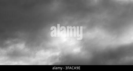 Dramatischer Himmel voller dunkler, wirbelnder Wolken. Sonnenlicht bricht in weichen, diffusen Strahlen durch. Die Stimmung ruft Vorfreude oder stürmischen Wandel hervor. Ideal für Stockfoto