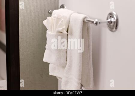 Weiße Handtücher hängen ordentlich auf einem schlanken Metallregal. Weiche Baumwolltextur unter sanftem Licht sichtbar. Minimalistisches Badezimmerdesign mit klaren Linien und neu Stockfoto