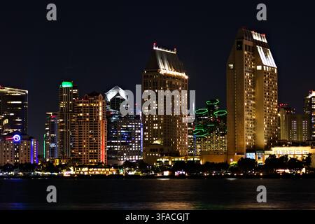 Nachtlichter leuchten auf hohen Stadthochhäusern. Wasser spiegelt leuchtende Gebäude unten wider. Städtische Skyline glänzt mit moderner Architektur. Grün und Gold Stockfoto