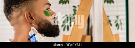 Ein junger afroamerikanischer Mann rasiert sich zu Hause und konzentriert sich auf seine Pflegeroutine. Stockfoto