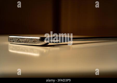 Horizontale Nahaufnahme eines Vintage-Stahlklingen-Putters, der auf einer reflektierenden Oberfläche mit warmer Low-Key-Studiobeleuchtung ruht. Stockfoto