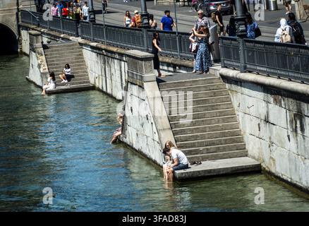 Einheimische und Touristen sitzen auf den Stufen entlang der Limmat und tauchen ihre Füße ins Wasser, um sich abzukühlen Stockfoto