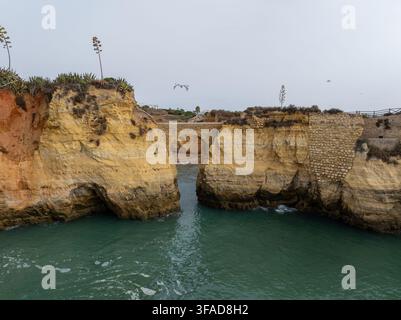 Luftaufnahme einer Steinbrücke, die zwei schroffe Klippen über einer türkisfarbenen Bucht in der Region Algarve, Bezirk Faro, Portugal verbindet Stockfoto