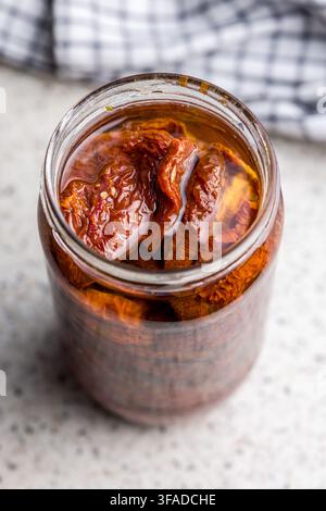 Glas mit in Öl eingelegten sonnengetrockneten Tomaten, das in einer Nahaufnahme auf einer Küchenoberfläche gezeigt wird und rustikale mediterrane Aromen und hausgemachte Vorratskammerzutaten hervorruft Stockfoto