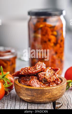 Sonnengetrocknete Tomaten in Olivenöl konserviert, serviert in einer Holzschüssel mit Gläsern und frischen Tomaten auf einem rustikalen Holztisch, der hausgemachtes Mittelmeer vermittelt Stockfoto