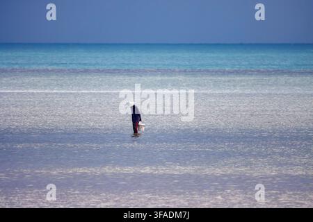 Ein örtlicher Fischer geht durch das flache Wasser bei Ebbe am Strand von Thong Krut, Koh Samui, Thailand. Stockfoto