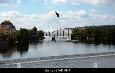 Prag, Tschechische Republik – Vltava mit historischer Brücke, Uferarchitektur und Stadtbild unter blauem Sommerhimmel. Stockfoto