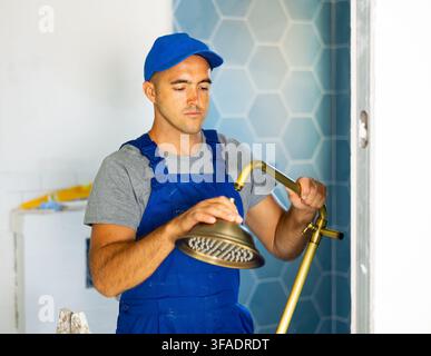 Junger Mann Baumeister in Arbeitskleidung arbeiten im Bad halten Duschkopf Stockfoto