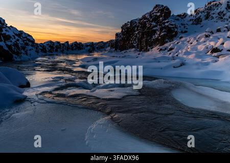 Winterszene im Freien mit einem schneebedeckten Fluss in der Nähe des teilweise gefrorenen Oxararfoss Wasserfalls im Thingvellir Nationalpark im Goldenen Kreis in Island. Stockfoto