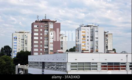 Mehrstöckige Wohnhochhäuser aus Betonblöcken und ein niedriges kommerzielles Gebäude stehen unter einem bewölkten Himmel in einem modernen Stadtviertel Stockfoto