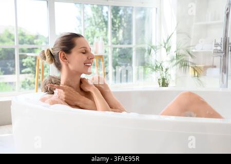 Selbstpflege und Wellness-Routine, glückliche Frau genießt ein entspannendes Schaumbad in einem hellen modernen Badezimmer Stockfoto