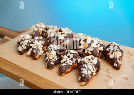Eine Gruppe von kleinen Croissants, teilweise mit reichhaltiger Schokolade überzogen und großzügig mit geschnittenen Mandeln bestreut, ist ordentlich auf einem Blatt ausgelegt Stockfoto