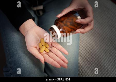Person, die gelbe Vitaminpillen aus einer Flasche in die Handfläche gießt für die tägliche Nahrungsergänzung Stockfoto