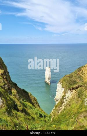 Atemberaubende Küstenlandschaft mit einer einsamen Kalksteinformation, die aus den ruhigen Meereswellen aufragt. Grüne Klippen rahmen die Aussicht unter einem vibrierenden Stockfoto