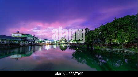 Lebendiger Sonnenuntergangshimmel mit lila und rosa Wolken, die sich auf dem ruhigen Flusswasser im Bezirk Shanhua, Tainan, Taiwan spiegeln. Stockfoto