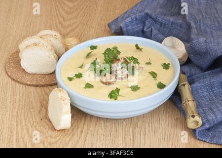 Cremige Pfifferlingssuppe in blauer Schale mit gebratenen Pilzen, Petersilie und Weißbrot auf hölzernem Hintergrund Stockfoto