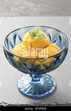 Mango-Eis mit Kokosmilch, verziert mit Minzblatt in blauer Glasschale auf dunkler Schieferplatte Stockfoto