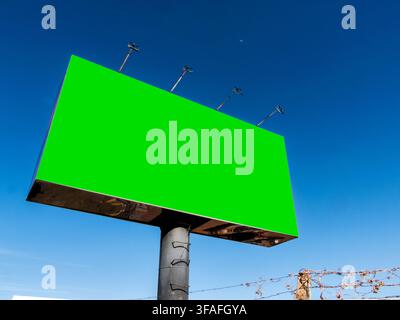 Großes leeres Werbeschild mit Chroma-Key-Grünhintergrundstruktur auf einem Metallpfahl unter einem klaren blauen Himmel, ideal für Außenwerbemockup, kommerziell Stockfoto