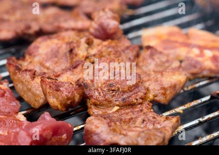 Marinierte Schweinehalssteaks braten auf einem Metallgrill mit aufsteigendem Rauch. Nahaufnahme von köstlichem gegrilltem Fleisch, das während eines Picknicks im Freien kocht Stockfoto