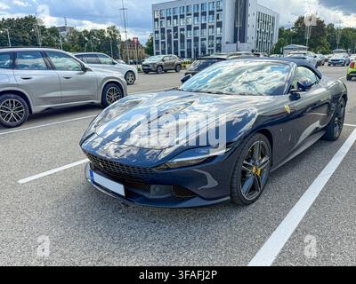 Riga, Lettland - 19. August 2026: Eleganter dunkelblauer Ferrari Roma Luxus-Sportwagen, der in einer modernen städtischen Umgebung geparkt ist und dramatische Wolken auf seinem polierten Stockfoto