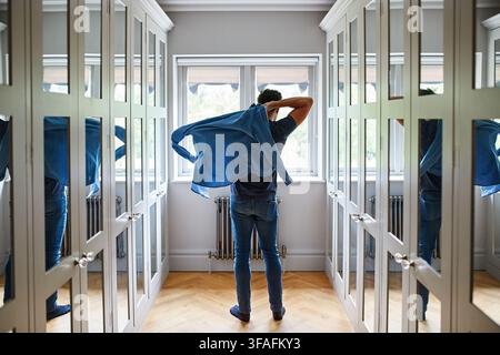 Mann, Fenster und Ankleide mit Hemd im Flur oder Schrank für Mode oder Vorbereitung zu Hause. Rückansicht, männliche Person oder sich im Korridor fertig machen mit Stockfoto
