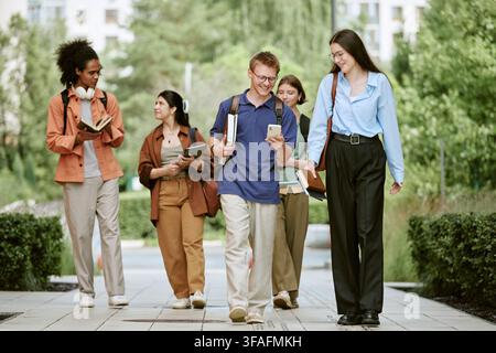 Verschiedene Gruppe von Studenten, die auf dem Campus spazieren und Smartphones nutzen Stockfoto