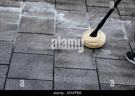 Mann reinigt schmutzige Patiofliesen mit einem Hochdruckreiniger im Freien, entfernt Moos und Schmutz von einem Wohnweg, Hauswartung, Außenreinigung Stockfoto