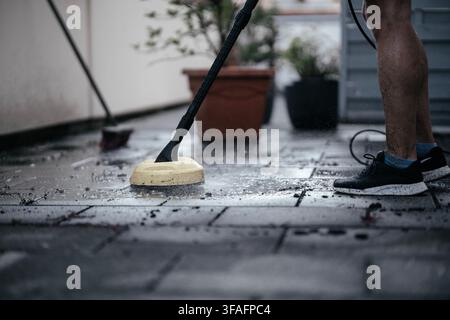Mann reinigt schmutzige Patiofliesen mit einem Hochdruckreiniger im Freien, entfernt Moos und Schmutz von einem Wohnweg, Hauswartung, Außenreinigung Stockfoto