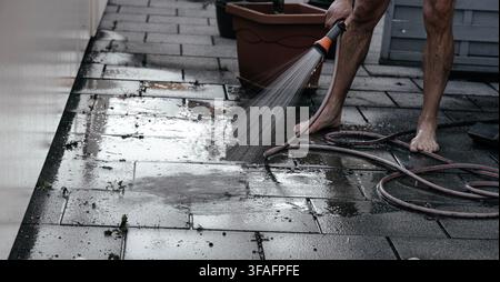 Mann reinigt schmutzige Patiofliesen mit einem Hochdruckreiniger im Freien, entfernt Moos und Schmutz von einem Wohnweg, Hauswartung, Außenreinigung Stockfoto
