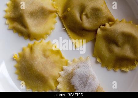 Überkopf-Makroaufnahme von rohen, handgemachten Kürbis-Tortelli mit gekräuselten Rändern, die mit Mehl bestäubt sind, eine traditionelle italienische Nudeln mit Füllung Stockfoto