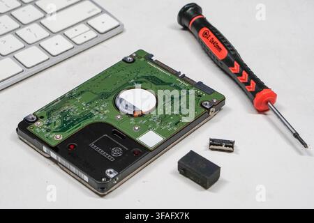 Demontierte Festplatte auf weißem Schreibtisch mit Präzisionswerkzeugen. Stellte IT-Wartung und Datenwiederherstellungsdienste dar. Stockfoto