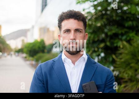 Selbstbewusster Geschäftsmann hält Smartphone vor einem modernen Büro Stockfoto