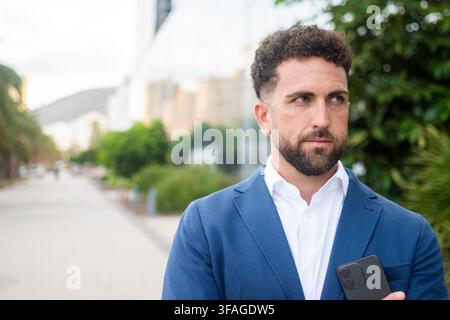 Selbstbewusster Geschäftsmann hält Smartphone vor einem modernen Büro. Kopierplatz. Stockfoto