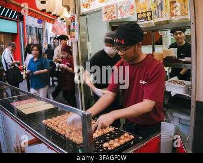 Verkäufer bereitet Takoyaki auf einer Grillplatte an einem Straßenimbiss in Dotonbori, Osaka, Japan zu Stockfoto