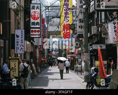 Fußgänger gehen durch eine enge Straße, die mit japanischen Restaurantschildern und Bannern in Osaka, Japan, gesäumt ist Stockfoto