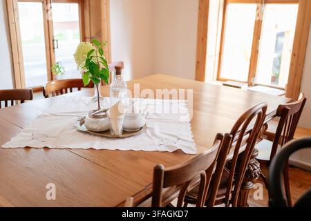 Gedeckter Esstisch für das Abendessen in einer häuslichen Innenumgebung, mit hölzernem Esstisch, Stühlen mit Holzrahmen, weißem Spitzentischläufer Stockfoto