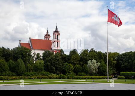 Kirche St. Philipp und St. Jakobs hinter dem Lukiškės-Platz in Vilnius, Litauen, neben der historischen Vytis-Flagge, die auf einem hohen Flaggenmast weht Stockfoto