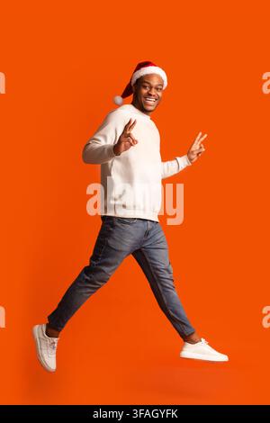 Festliche Freude. African Guy In Santa Hat Mit Spaß Über Orange Hintergrund Stockfoto