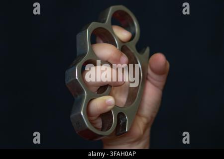 Eine Nahaufnahme zeigt eine Kinderhand, die fest Metallknöchelhalter gegen einen dunklen Hintergrund hält. Stockfoto