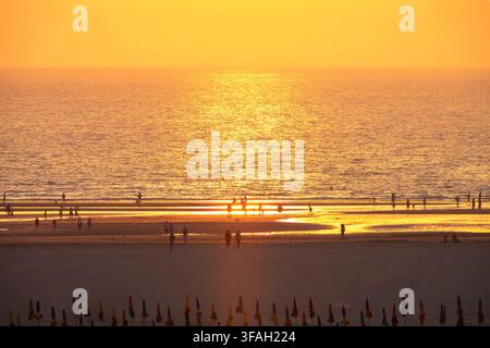 Silhouetten von Menschen und Sonnenschirmen am Strand von Deauville bei Sonnenuntergang im Sommer, Normandie, Frankreich. Luftaufnahme und goldenes Sonnenlicht Stockfoto