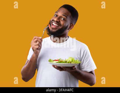 Fröhlicher Schwarzer Kerl Essen Salat Genießen Gesunde Mahlzeit, Gelber Hintergrund Stockfoto