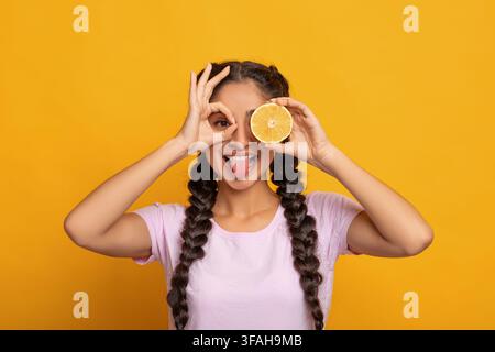 Indische Dame lächelnd, Blick auf die Kamera durch Finger und Obst Stockfoto