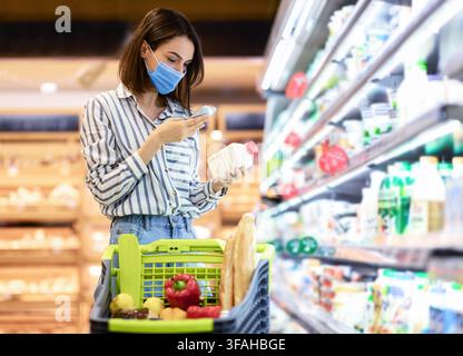 Frau in Maske Scannen Code auf Produkten mit Smartphone Stockfoto